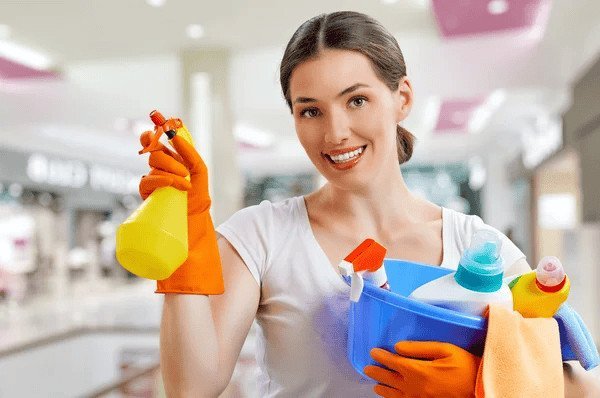Smiling woman holding cleaning products and a spray bottle.